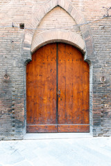 Ancient wooded double doors in a brick wall with decorative arch