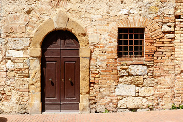 Fototapeta na wymiar Dark wooden double doors in an ancient stone wall, with a window with bars on it