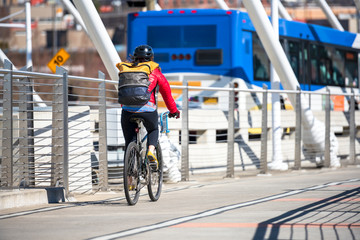 Woman with backpack and jacket rides bike on the bridge next to the bus preferring healthy lifestyle