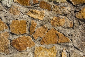 old wall of yellow stones of various sizes and shapes in gray cement. rough surface texture