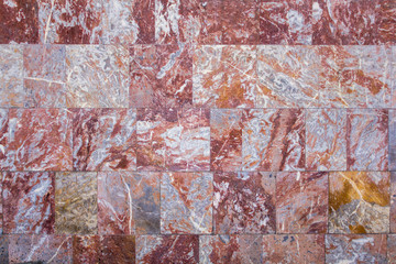 wall of red marble granite tiles with white and gray spots. rough surface texture