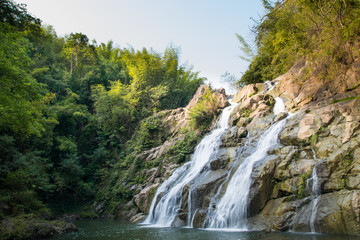Naklejka na ściany i meble Beautiful large waterfall flowing between rocks in a deep green forest. Waterfall flowing over rocks. Nature background.