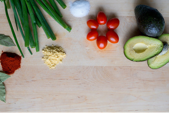 Background picture with vegetables in. Green onions, cherry tomato, avocado, bay leaves, mustard, parika and salt on the wooden cutting board in the kitchen.