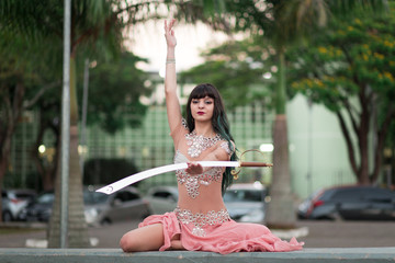 A beautiful belly dancer in the park with a sword