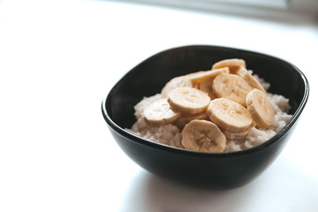 Rice milk porridge with banana in a black plate on a white background