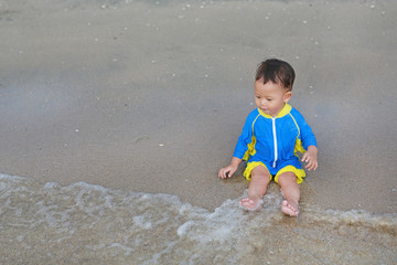 Portrait of Asian baby boy in swimming suit sitting on the sand beach.
