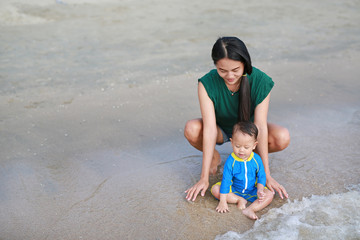 Asian mother and baby boy playing water on beach.