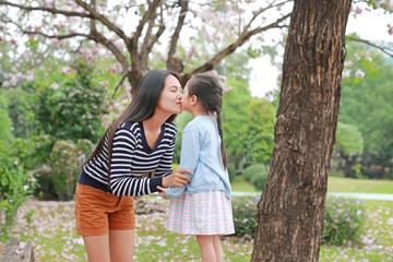 Happy mom kissing her daughter in garden with fully fall pink flower around outdoor.