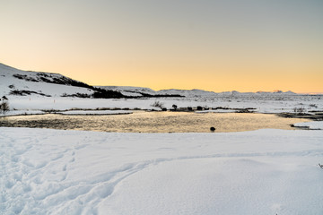 Fototapeta na wymiar Water flowing through snowy, icy landscape just before sun rise with mountains in the background
