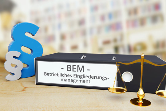 Betriebliches Eingliederungsmanagement (BEM) – Gesetz/Recht. Ordner auf Schreibtisch mit Beschriftung neben Paragraf und Waage. Anwalt