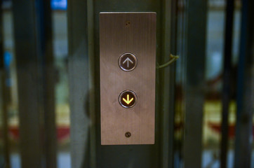 Elevator button to go up and down with arrows. The button is placed on a polished stainless steel plate. The orange light is switched on the sign that requests to go downstairs.