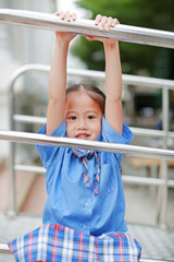 Fototapeta premium Smiling little Asian girl in school uniform playful hanging at metal stair.