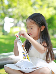 Smiling little Asian child girl playing stickers in the green park.