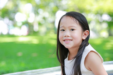 Portrait of smiling little Asian child girl in sunny green park.