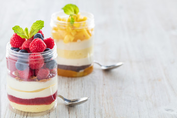 Raspberry and mango dessert, cheesecake, trifle, mouse in a glass jar on a light wooden background