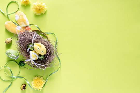Colourful Easter eggs in birds nest with festive decoration on bright lime green background, top view- image