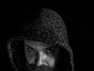 portrait of a man with a beard and mustache in the hood with a serious face on a black background.black and white photo