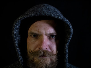 Fototapeta premium portrait of a man with a beard and mustache in the hood with a serious face on a black background