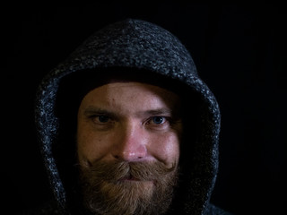 portrait of a man with a beard and mustache in the hood with a smiling face on a black background