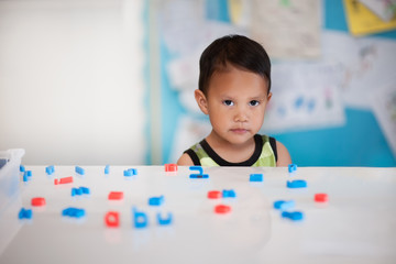 Young boy having difficulty learning in a kindergarten room with alphabet letters on the desk.