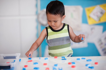 A smart young boy manipulating alphabet letters to form words in kindergarten room.