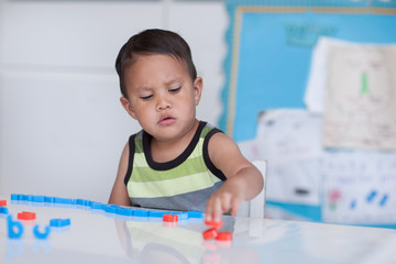 A young boy with an upset facial expression, grabbing alphabet letters from the desk and making a pattern in a classroom setting.
