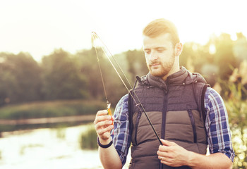 Fisherman with a spinning and bait catching fish on a lake or river. Man on a weekend with a fishing road. Hobby and leisure concept.