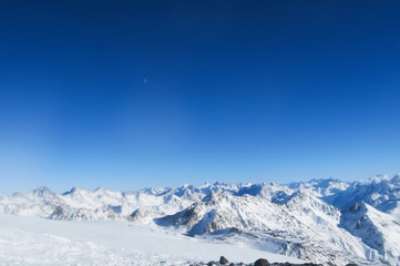 Moon above the snowy glacier of Caucasian Mountains in the blue sky. Elbrus region