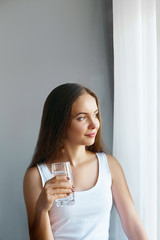 Healthy lifestyle. Young woman show glass of water. Girl drinks water. Portrait of happy smiling female model  holding transparent glass of water. Health,Beauty, Diet concept