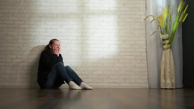 Depressed man is crying while sitting on the floor near the wall at home alone.