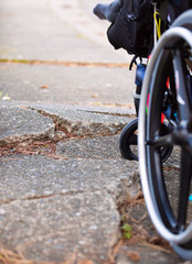 Wheelchair wheels up against cracks in broken sidewalk