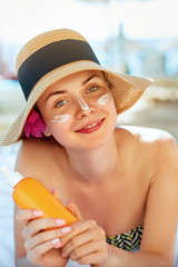 Skincare. Beauty Concept. Young pretty woman holding  sun cream and applying on her face. Female in hat smear  sunscreen lotion on skin and touch own face. Skin Protection and dermatology.