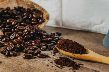 Roasted coffee beans in sacks and crushed coffee with a hand cranked coffee grinder were poured into a spoon on an old wooden table.