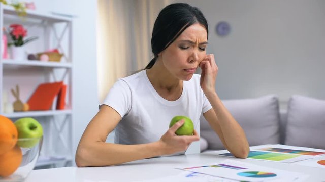 Female designer working at home feeling dental pain while biting fresh apple