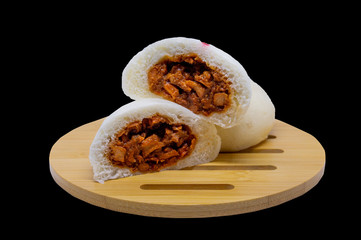 Steamed buns with red pork filling on a wooden tray and a black background