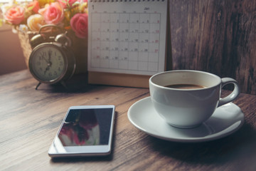 Cup of Coffee,mobile phone with Desktop Calendar 2019vintage clock and pot of rose flower on blue wooden desk,Working space at home,Urban Lifestyle concept