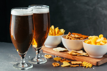 Glass of lager beer with snack bowls on dark stone background