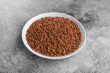 Buckwheat cereal in a white saucer on a gray concrete background