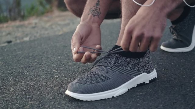 Close up shot of a young white male runner tying his shoes and standing up admiring the view before his run