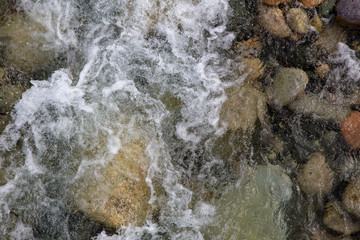 Water in the mountain raging river. Beautiful natural background of stones and water. Texture of clear water and fast river. Background to insert text. Tourism and travel.