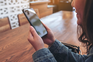 Closeup image of an asian woman holding , using and looking at smart phone in cafe