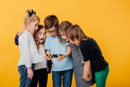 group of children, are scared look at the phone, isolated yellow background, copy space