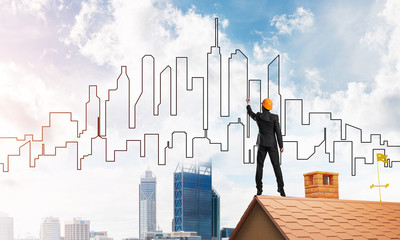 Man architect draw silhouette of modern city on blue sky. Mixed media
