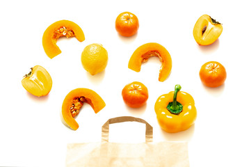orange vegetables and fruits in paper bag on white background. pumpkin, lemon, Tangerine, persimmon, yellow pepper