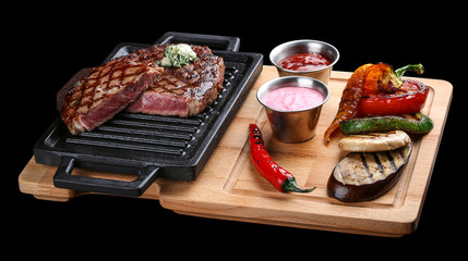 Rib eye steak on wooden tray with grilled vegetables on dark background