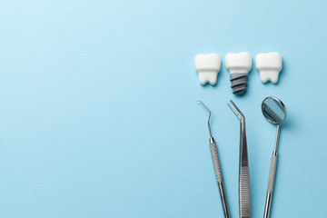 Healthy white teeth and implants on blue background and dentist tools mirror, hook. Copy space for text.