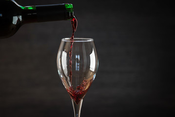 Pouring red wine into the glass against wooden background