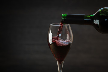 Pouring red wine into the glass against wooden background