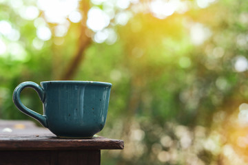 green mug of hot drink put on wooden table in nature of morning day