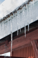 Sharp icicles and melted snow hanging from eaves of roof. Beautiful transparent icicles slowly gliding of a roof.